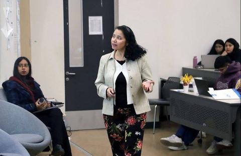 Una mujer presenta un tema mientras un grupo de estudiantes la observa en un aula.