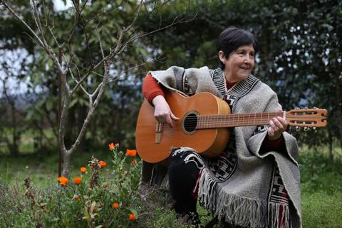 Una mujer sentada en el jardín, tocando la guitarra y rodeada de flores naranjas.