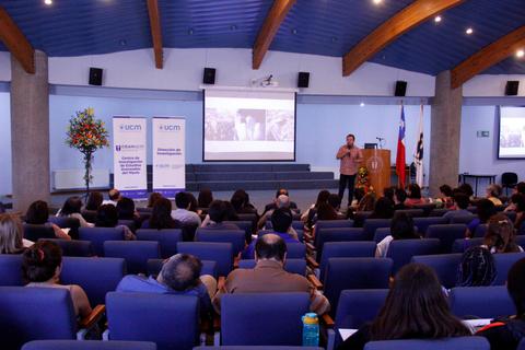 Una conferencia en un salón con un orador frente a una audiencia sentada.