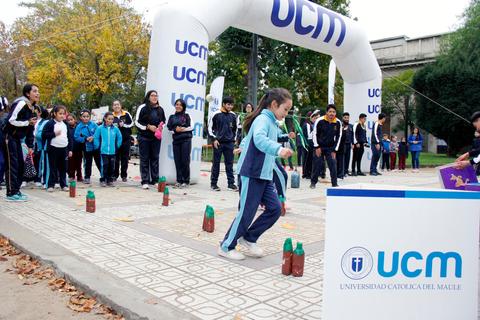 Un grupo de niños y adultos participan en una actividad deportiva al aire libre en un evento de la Universidad Católica del Maule.