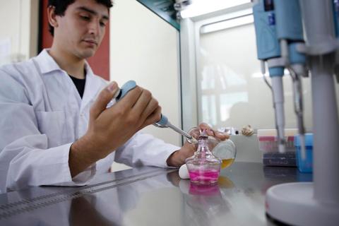 Un joven en un laboratorio mezcla líquidos en frascos utilizando un micropipete.