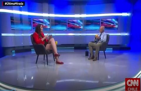 Una conversación en un set de televisión con dos personas sentadas, una de ellas en un vestido rojo y la otra en una camisa azul.