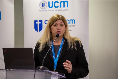 Una mujer dando una charla en una conferencia, detrás de un podio con un micrófono.