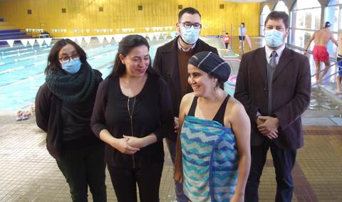 Un grupo de personas, incluyendo una nadadora, se encuentran en una piscina mientras conversan sonrientes.