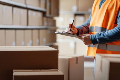 Un trabajador en un almacén revisa su lista mientras se encuentra rodeado de cajas de cartón.