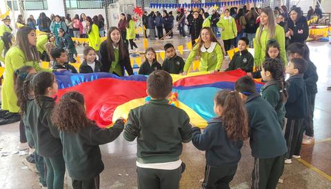 Un grupo de niños y adultos sosteniendo una bandera colorida en un ambiente festivo.