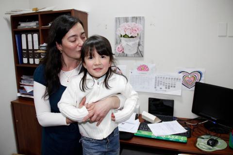 Una madre abraza a su hija pequeña en un entorno de oficina.