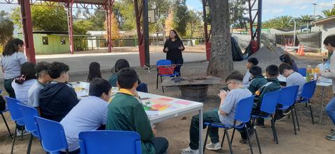 Un grupo de estudiantes escucha atentamente a una persona que les está hablando al aire libre.