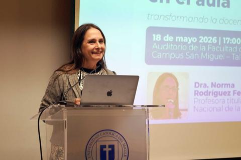 Una mujer sonriente presenta en un auditorio universitario.