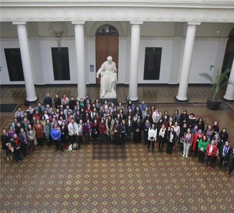 Un gran grupo de personas se reúne en un patio interior con columnas y una estatua al fondo.