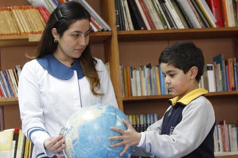 Una profesora le muestra a un niño un globo terráqueo en una biblioteca.