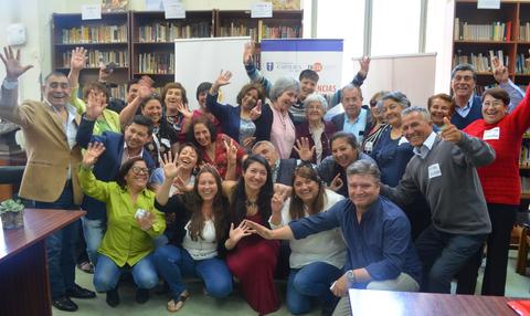 Un grupo de personas sonrientes y levantando las manos en un evento comunitario.