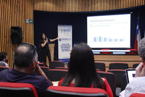 Una presentadora expone un tema frente a un público en un evento académico.