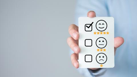Una persona sostiene una tarjeta con caras que evalúan la satisfacción del cliente.