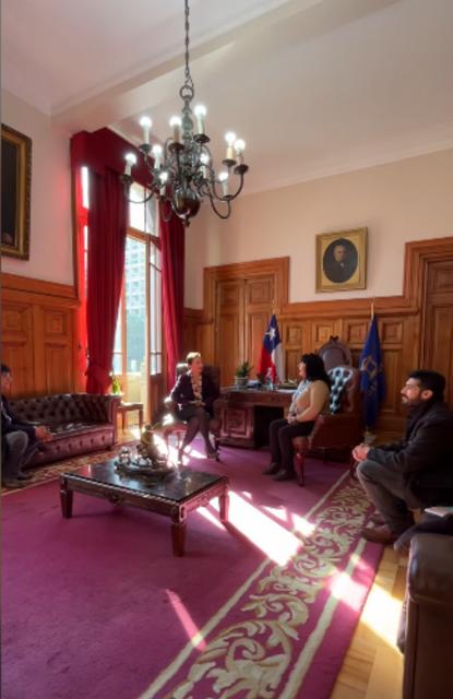 Una reunión en una sala elegante con grandes ventanales y decoración clásica.