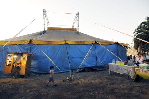 Un niño juega cerca de una carpa de circo azul y amarilla en un ambiente al aire libre.