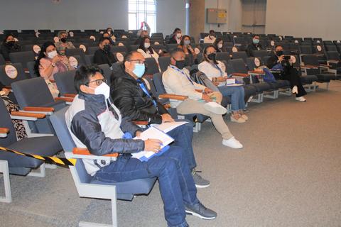Un grupo de personas sentadas en una sala, usando mascarillas, durante una reunión o evento.
