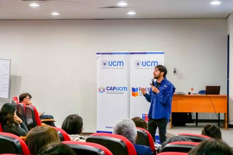Un hombre con barba y gafas presenta frente a un público en un auditorio.