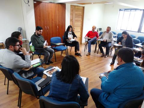 Un grupo de personas participa en una reunión sentados en sillas alrededor de una mesa.