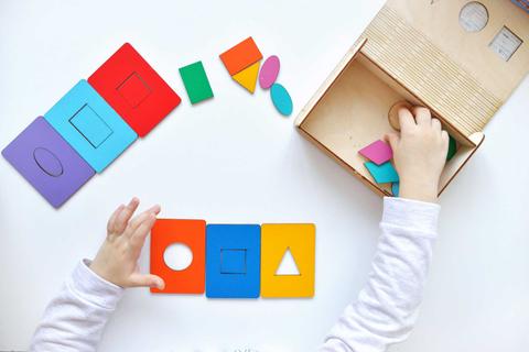 Un niño juega con formas geométricas de colores sobre una mesa.