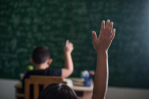 Un niño en un aula levanta la mano para responder a una pregunta.