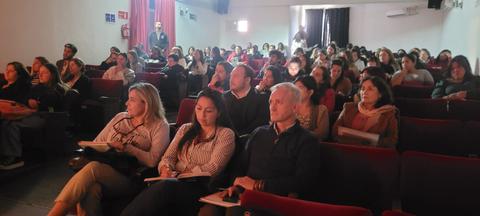 Una multitud de personas sentadas en un auditorio, prestando atención a una presentación.