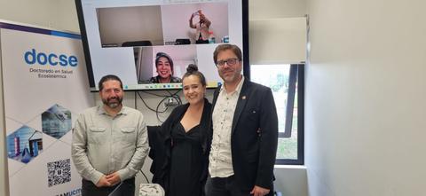 Fotografía de un grupo de personas en una sala de conferencia con una pantalla que muestra una videollamada.