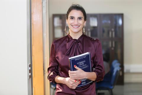 Una mujer sonriente sostiene un libro titulado 'Código Civil' en un entorno de oficina.