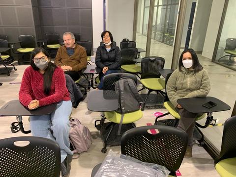 Un grupo de personas sentadas en un aula vacía con escritorios verdes.