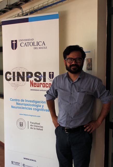 Un hombre posa frente a un banner de una universidad y un centro de investigación en neurociencia.