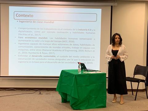 Una mujer se presenta frente a una pantalla con texto sobre el contexto de ingeniería en la industria 4.0.