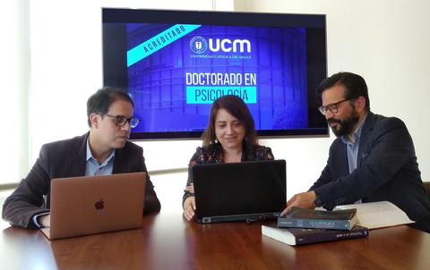 Tres personas están reunidas frente a una pantalla que presenta el programa de Doctorado en Psicología de la UCM.