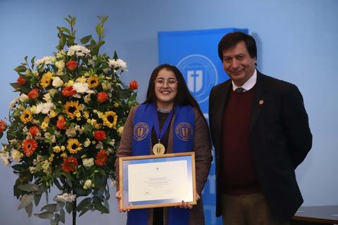 Una estudiante sonriente recibe su reconocimiento en una ceremonia académica junto a un profesor.