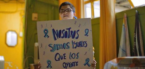 Un niño sostiene un cartel que dice 'Nosotros somos iguales que los oyentes'.