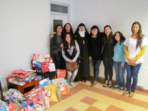 Un grupo de mujeres junto a una monja se encuentra en una habitación con paquetes de regalos a su alrededor.