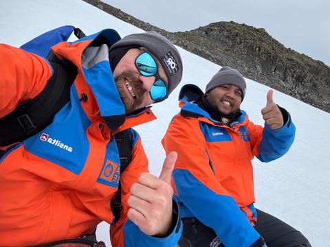 Dos personas sonrientes en la nieve, vistiendo chaquetas de colores brillantes.