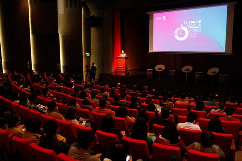 Una conferencia se está llevando a cabo en un auditorio lleno de asistentes sentados en sillas rojas.