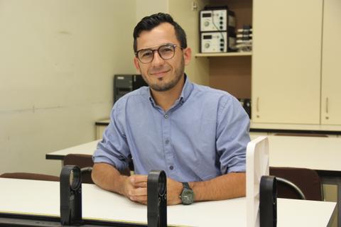 Un hombre sonriente con gafas sentado en una mesa de trabajo.