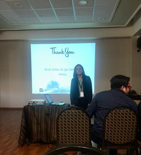 Una mujer de pie frente a una presentación en una sala de conferencias agradeciendo a la audiencia.