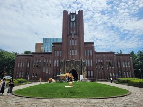Una imponente edificación con un reloj en su torre, rodeada de césped y personas en el exterior.