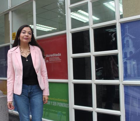 Una mujer con chaqueta rosa posa frente a una pared de vidrio con colores distintos.