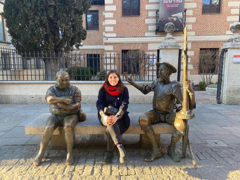 Una mujer sentada entre dos estatuas de bronce en un banco en la calle.