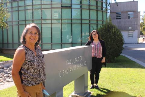 Dos mujeres posan frente a un edificio de la Facultad de Ciencias de la Salud.
