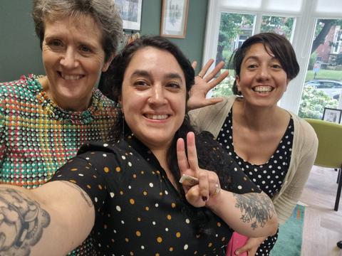 Tres mujeres sonríen en una foto grupal dentro de un ambiente luminoso y decorado.