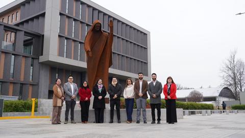 Un grupo de personas posando frente a una escultura en un entorno urbano.