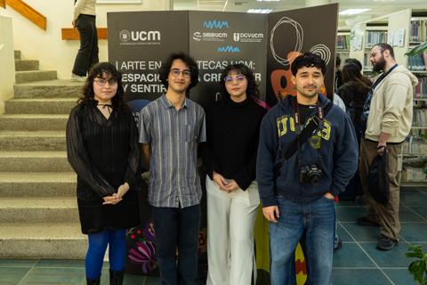 Un grupo de cuatro jóvenes posando en un evento cultural con una decoración artística al fondo.
