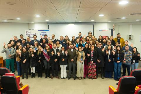 Un grupo grande de personas sonriendo y saludando en un evento en Chile.