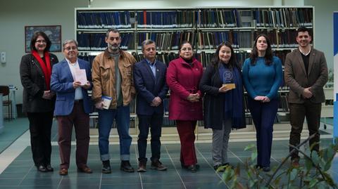 Un grupo de ocho personas posando en un ambiente académico, rodeados de estanterías llenas de libros.