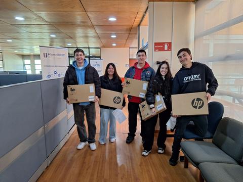 Un grupo de cinco personas sostiene cajas de laptops en un ambiente interno.