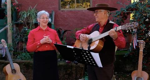Un hombre y una mujer están en un escenario al aire libre, él toca la guitarra y ella parece estar disfrutando de la música.
